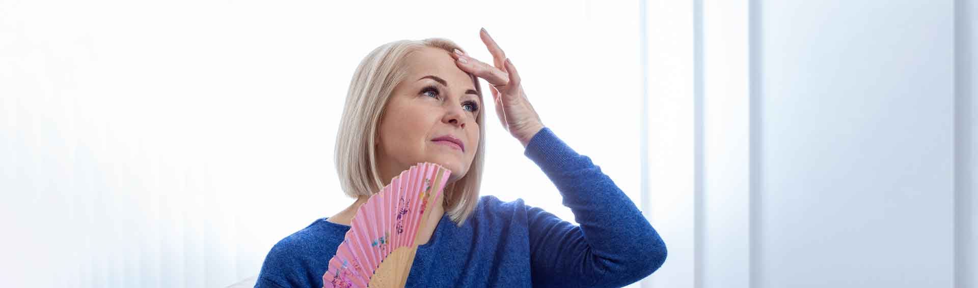 A woman trying to cool herself down with a foldable fan.