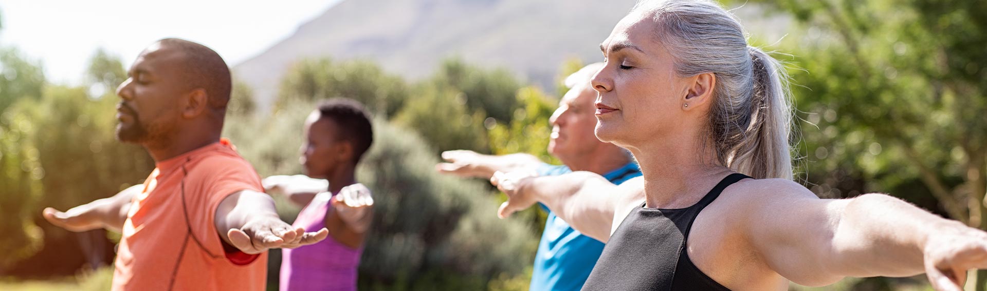 Friend group doing yoga outdoors, with mountains visible in the background.