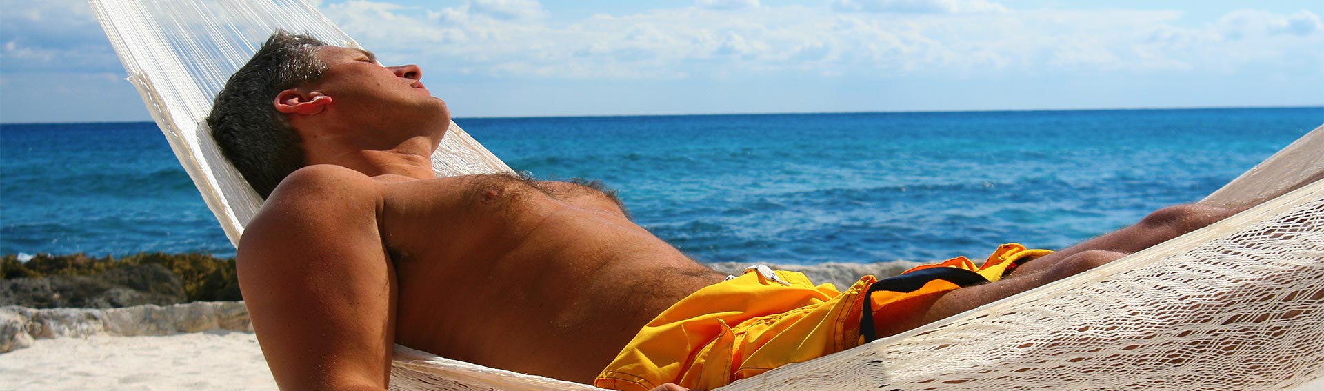 A man lounging in a hammock near the beach during the Summer.