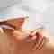 Woman applying Pevonia Hydrating Sunscreen at the beach on a bright, sunny day.