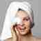 Teenage girl with a towel wrapped around her hair, covering one eye with a circular cotton pad.